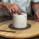 A cake decorated to resemble a roll of toilet paper on a wooden lazy susan with chef's hand holding down the center